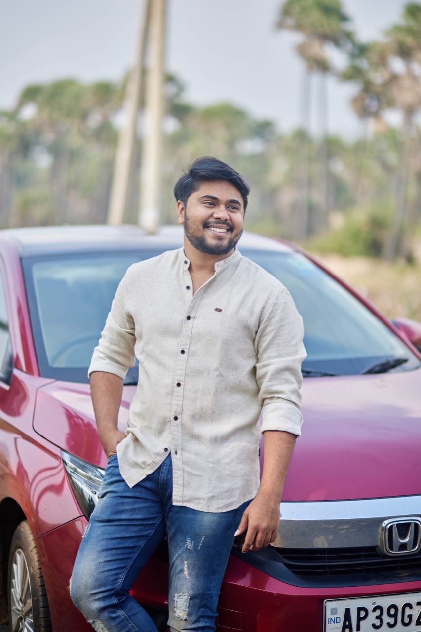 Rohith Siddela smiling and leaning against a red Honda car, with palm trees in the background.